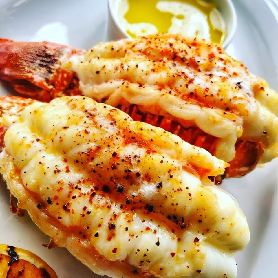 Two grilled lobster tails with seasoning, served with a side of melted butter.