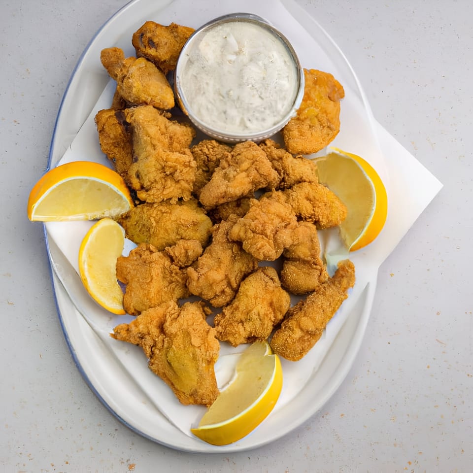 A white platter filled with golden-brown fried chicken pieces, lemon wedges, and a side of dipping sauce.